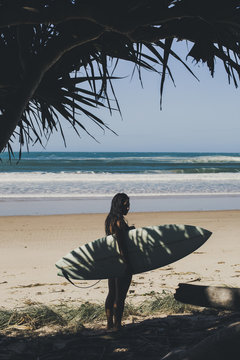 A young female surfer holding a surfboard in the shade