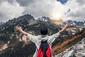Tourist with hands up stands on the background of a mountain landscape.