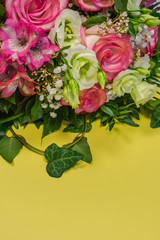Close up view of a bunch or a bouquet of pink roses, pink Alstroemeria and white Lisianthus flowers  on a yellow background with copy space