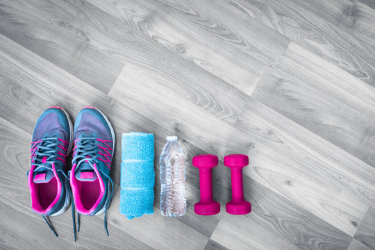 Fitness, workout, and gym concept. Sneakers towel water bottle and weights against wooden background.  