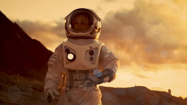 Female Astronaut Checks Data on Her Wrist Computer while Exploring Alien Red Planet/ Mars. Space Travel, Planet Colonization Concept. Shot on RED EPIC-W 8K Helium Cinema Camera.