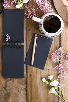 Aramatic coffee in a mug. Planning the day in a black notepad. Decor of pink flowers on a wooden table. Free space for text. Card.