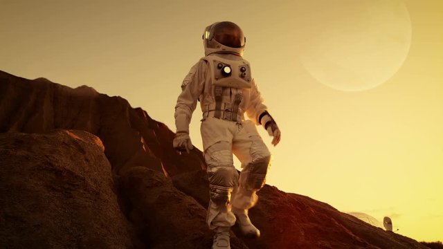 Brave Astronaut Descents from the Mountain on the Alien Red Planet/ Mars. Space Exploration/ Travel, Colonization Concept. Shot on RED EPIC-W 8K Helium Cinema Camera.