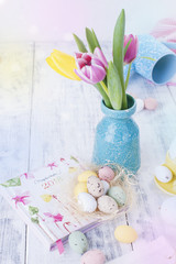 A small bouquet of pink tulips in a blue vase. Easter decor. White wooden background for text.