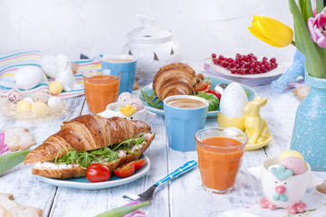 A family breakfast of croissants with rocket salad and cheese and aromatic coffee. Fresh tulips of pink color and eggs of different colors and Easter decor, ceramic rabbits. Free space for text.