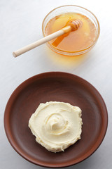 Sour cream, cottage cheese, dairy product in a clay bowl, cottage cheese on a white background in rustic style, honey and wooden stick, cream in a brown plate, French breakfast, copy space, minimalism