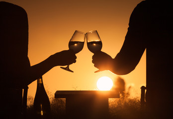 Couple celebrating outdoors with a glass of wine and beautiful sunset.  Happy life moments, romance, concept. 