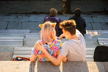 Young millennial couple on the waterfront, on the head of the girl's ears a character of Japanese...