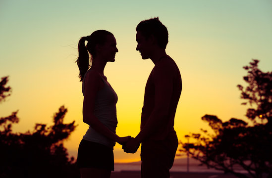 Affectionate couple holding hands standing against a beautiful sunset. Love and relationships concept.