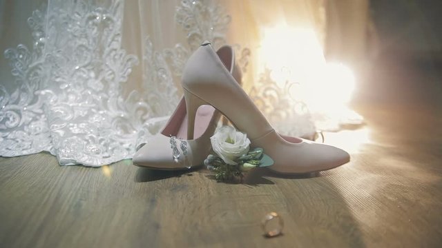 Two wedding rings rolling together near bride's wedding shoes