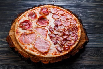 Appetizing pizza with bacon, salami,ham and pepperoni served on chopped wood, close up. Italian food, restaurant menu