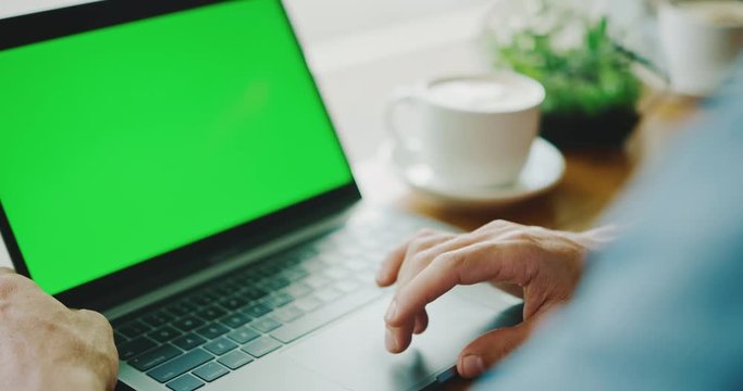 Man working on laptop with green screen in coffee shop