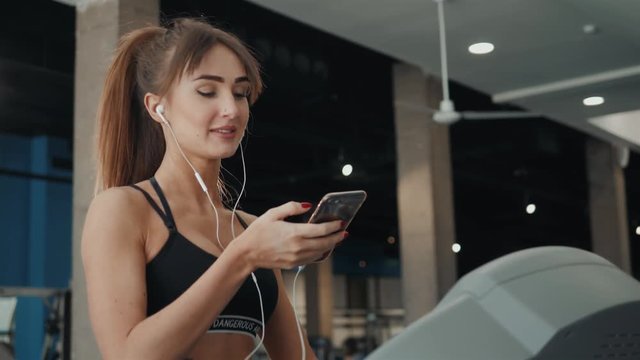 pretty young woman athlete with smartphone running on treadmill in gym, woman girl listening music on mobile phone text message speech recognition command cell phone voice