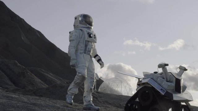 Astronaut Goes on the Expedition to Explore Rocky Alien Planet. In the Background His Base and AI Powered Rover. Futuristic Colonization Concept. Shot on RED EPIC-W 8K Helium Cinema Camera.