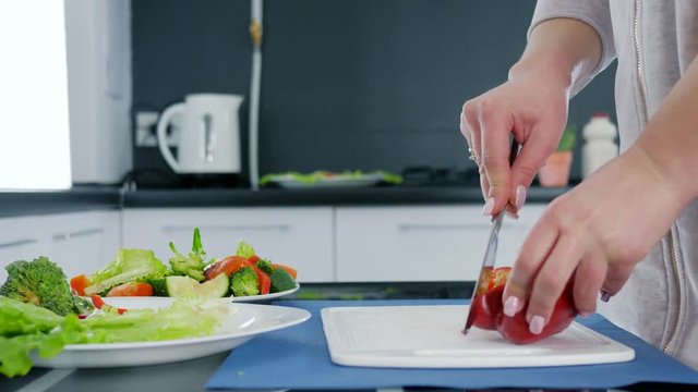 hands of woman with knife slicing sweet red pepper for salad on a cutting board, healthy food