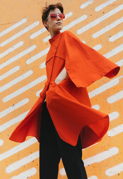 Urban stylish short hair female model in red/orange coat in front of orange background.