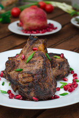 Steak on ribs, cooked on a grill with pomegranate on a white plate. Wooden rustic background. Top view