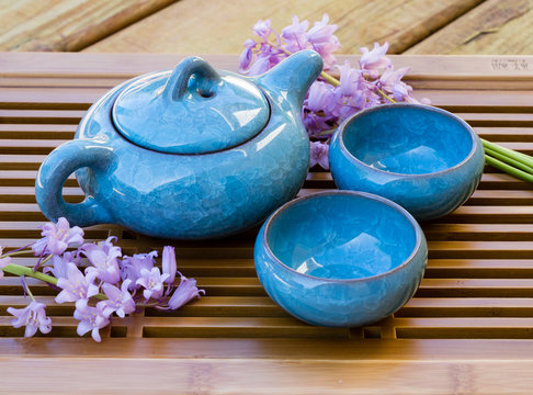 Blue ice crackle glazed ceramic tea pot with two tea cups on a tray decorated with flowers
