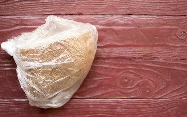 A piece of black bread in a polyethylene bag on a claretish wooden background. The concept of...