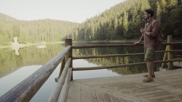 a young man with a camera goes to the lake in the mountains and smokes