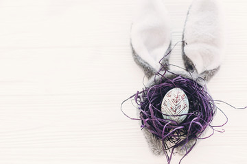 bunny ears and stylish egg in nest on white wooden background in light with space for text. creative easter image. season's greeting card mock-up. happy easter concept