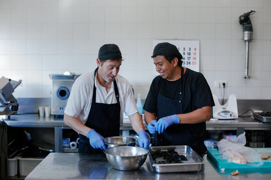 Two cooks working together with a very good mood in a restaurant kitchen preparing mussels