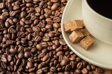 scattered grains of coffee on a wooden table with a white cup of coffee