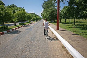 Obraz premium Lady cycles down a deserted road in Bagan, Burma
