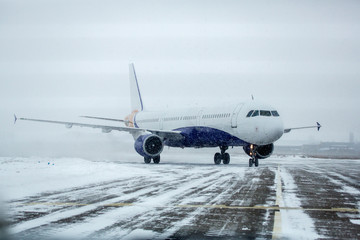 Airliner on runway in blizzard. Aircraft during taxiing at heavy snow. Passenger plane in snow at...
