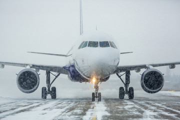 Airliner on runway in blizzard. Aircraft during taxiing at heavy snow. Passenger plane in snow at...