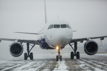 Airliner on runway in blizzard. Aircraft during taxiing at heavy snow. Passenger plane in snow at airport. Modern twin-engine passenger airplane taxiing for take off at airport during snow blizzard