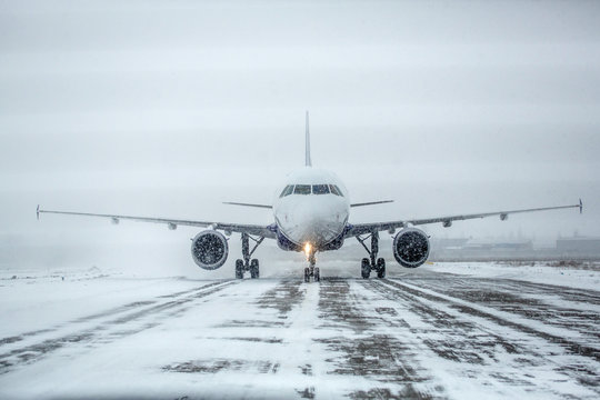Airliner on runway in blizzard. Aircraft during taxiing at heavy snow. Passenger plane in snow at airport. Modern twin-engine passenger airplane taxiing for take off at airport during snow blizzard