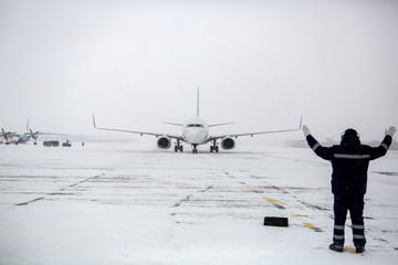 Member of ground crew park passenger airliner on airport apron in blizzard. passenger airliner taxi...