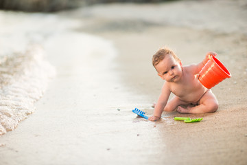 Cute caucasian baby girl play with sand on beach, looking at camera