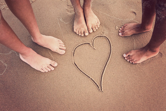 Racially diverse children's feet at the beach with a heart drawn in the sand