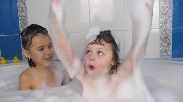 Children in the bathroom. Little girls play with foam in the bath.