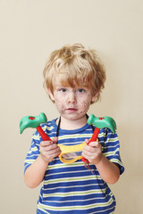 Silly young boy holding toy hammers with scribbling on his face