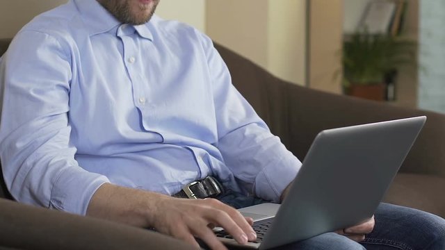 Male sitting on couch and typing e-mail on laptop computer, freelance job