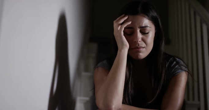 4K Panning shot of sad, emotionally vulnerable woman sitting alone in darkness