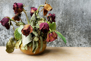 Dry roses in a vest on wooden table with old stain background, selective focus