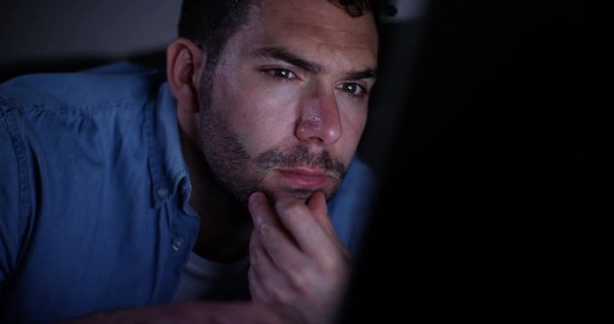 4K Close up on face of tired or unhappy man looking at laptop late at night