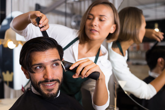 female professional shaving cheerful male's hair