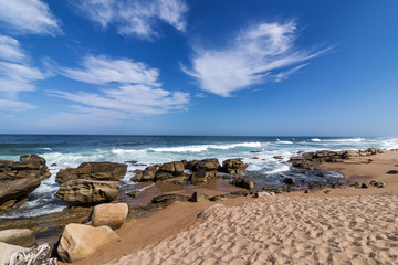 Fototapeta na wymiar Blue Cloudy Beach Sand Rocks and Ocean Waves Seascape
