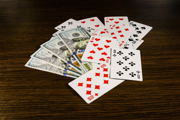 Playing cards and one hundred dollar bills on a dark wooden table