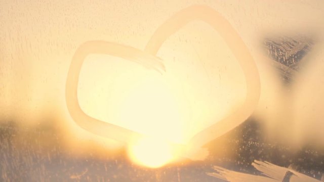Drawn heart on frost car window against sunset road in snow winter romantic mood