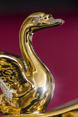 Golden figurine of a single swan close-up on a red background.