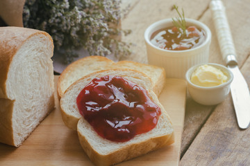 Delicious toast bread served with butter and spread with strawberry jam on wood cutting board put on rustic wooden table with copy space. Homemade bakery concept. American breakfast style.