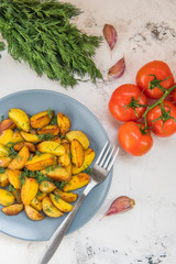 Fried potatoes in a plate. Baby potatoes, green, tomatoes and garlic on the table