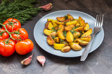 Fried baby potatoes, green, tomatoes and garlic on a dark background