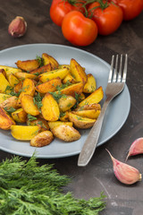 Fried baby potatoes, green, tomatoes and garlic on a dark background
